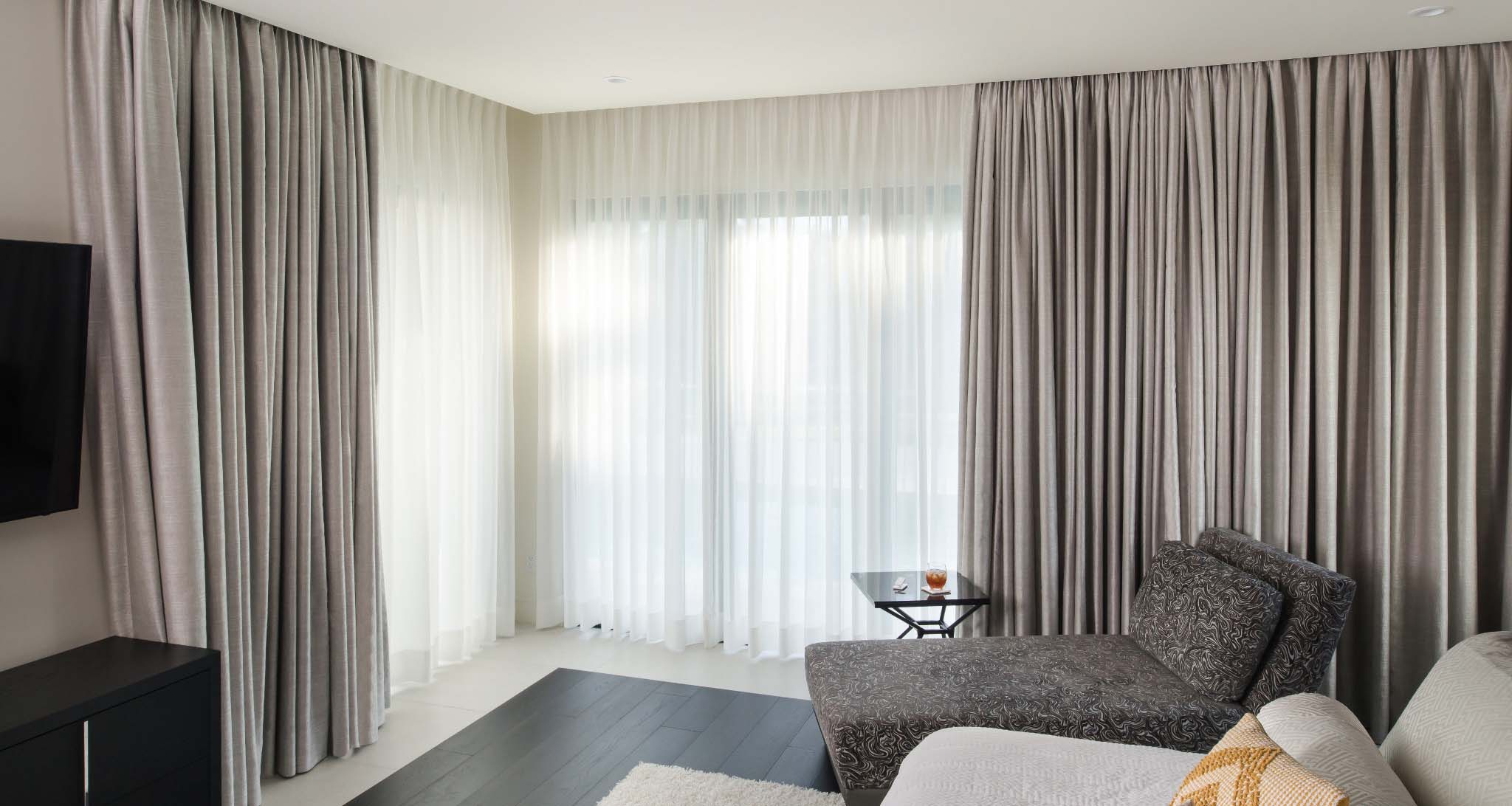 Layered sheer and blackout floor to ceiling curtains in a minimalist bedroom