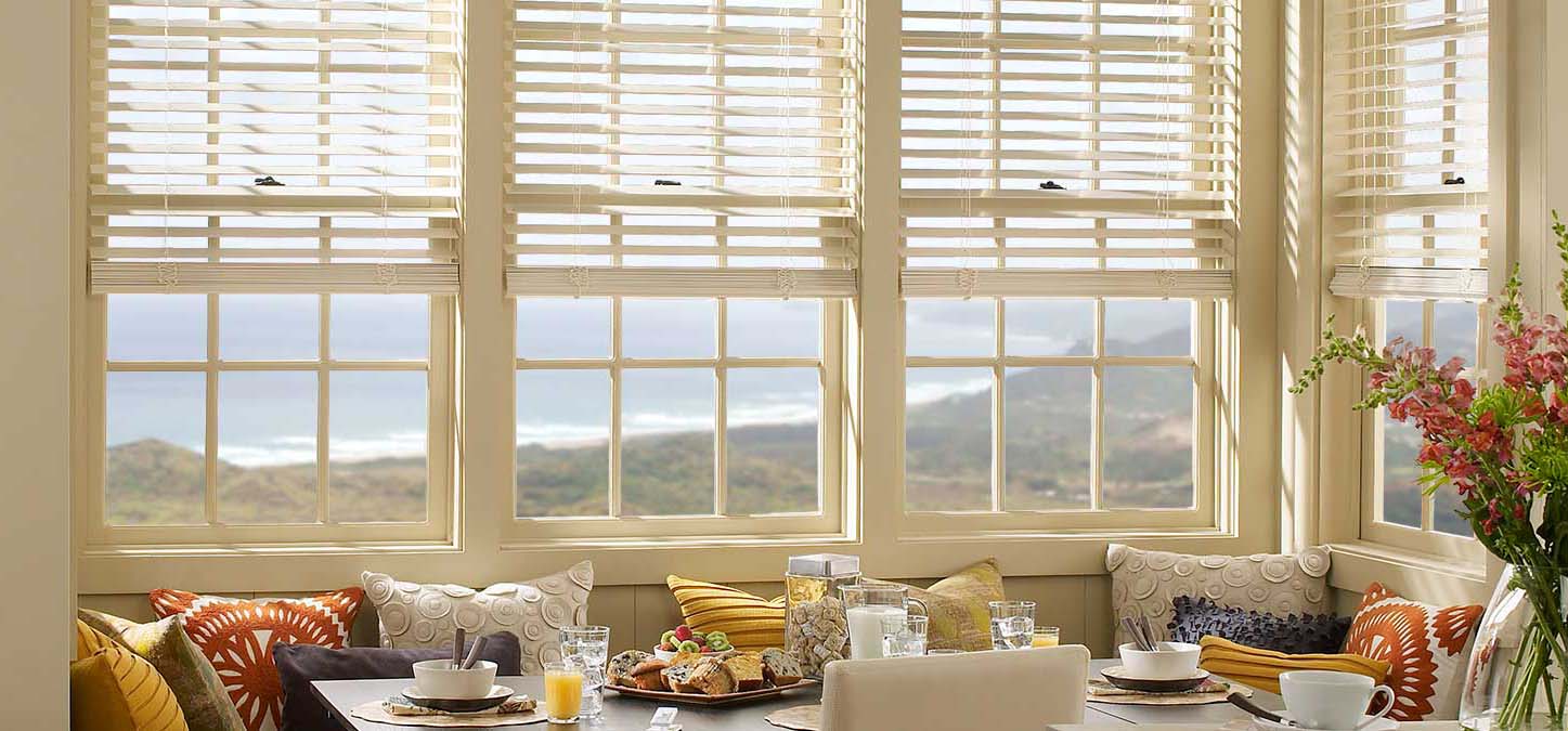 Wooden horizontal blinds on sunlit windows above a breakfast nook with pillows