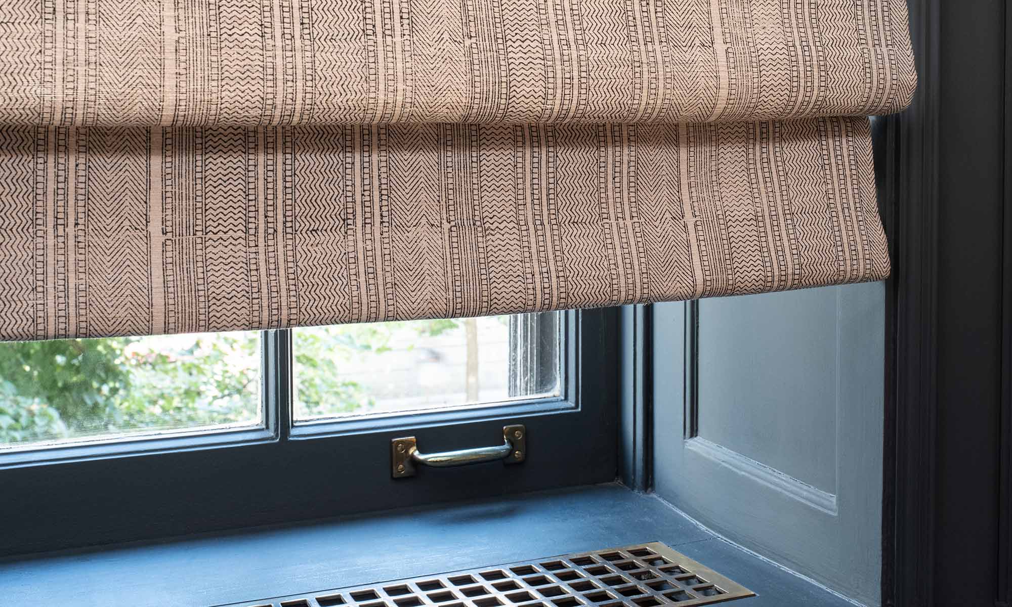 Close up of a textured fabric roman shade partially covering a window