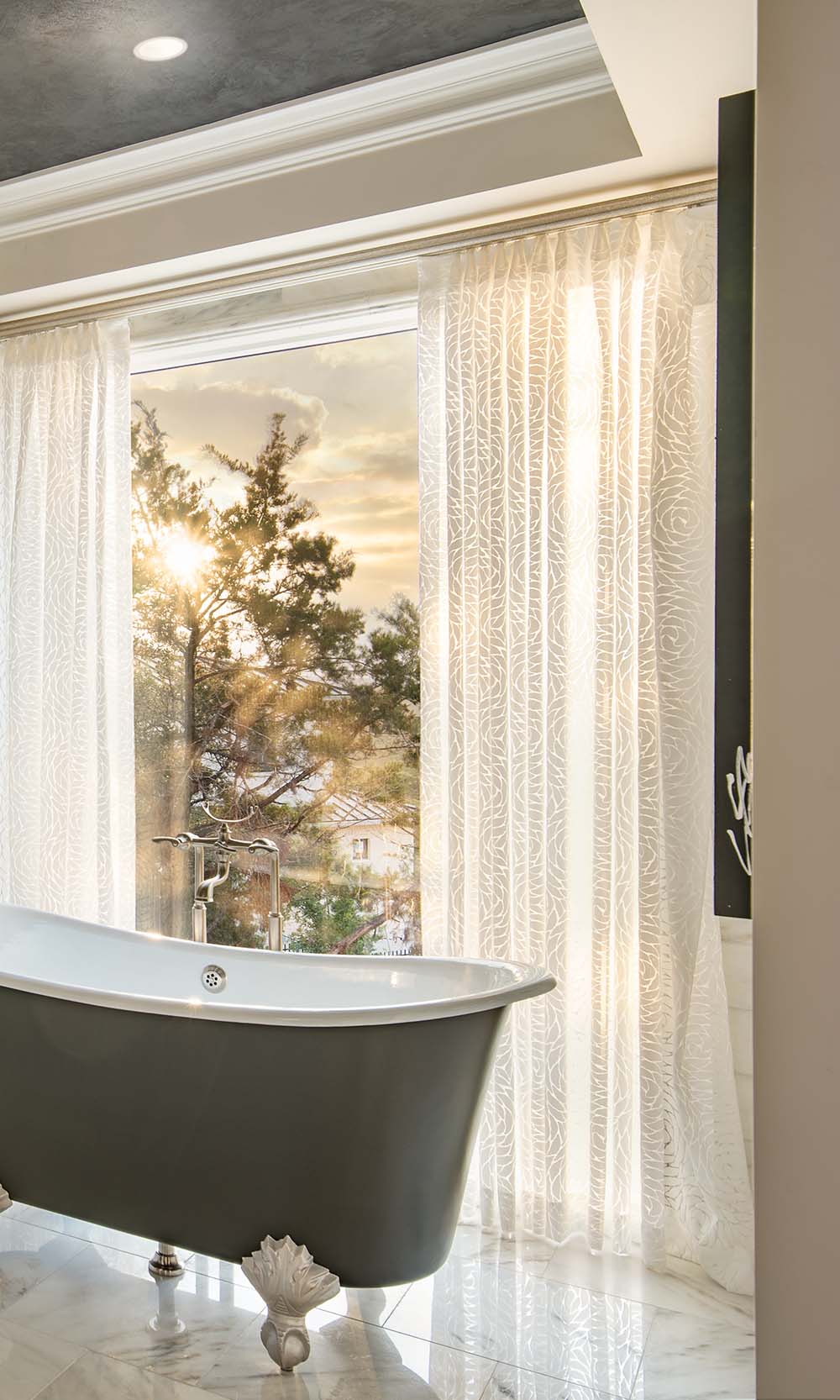 Patterned sheer white curtains beside a freestanding bathtub at sunset