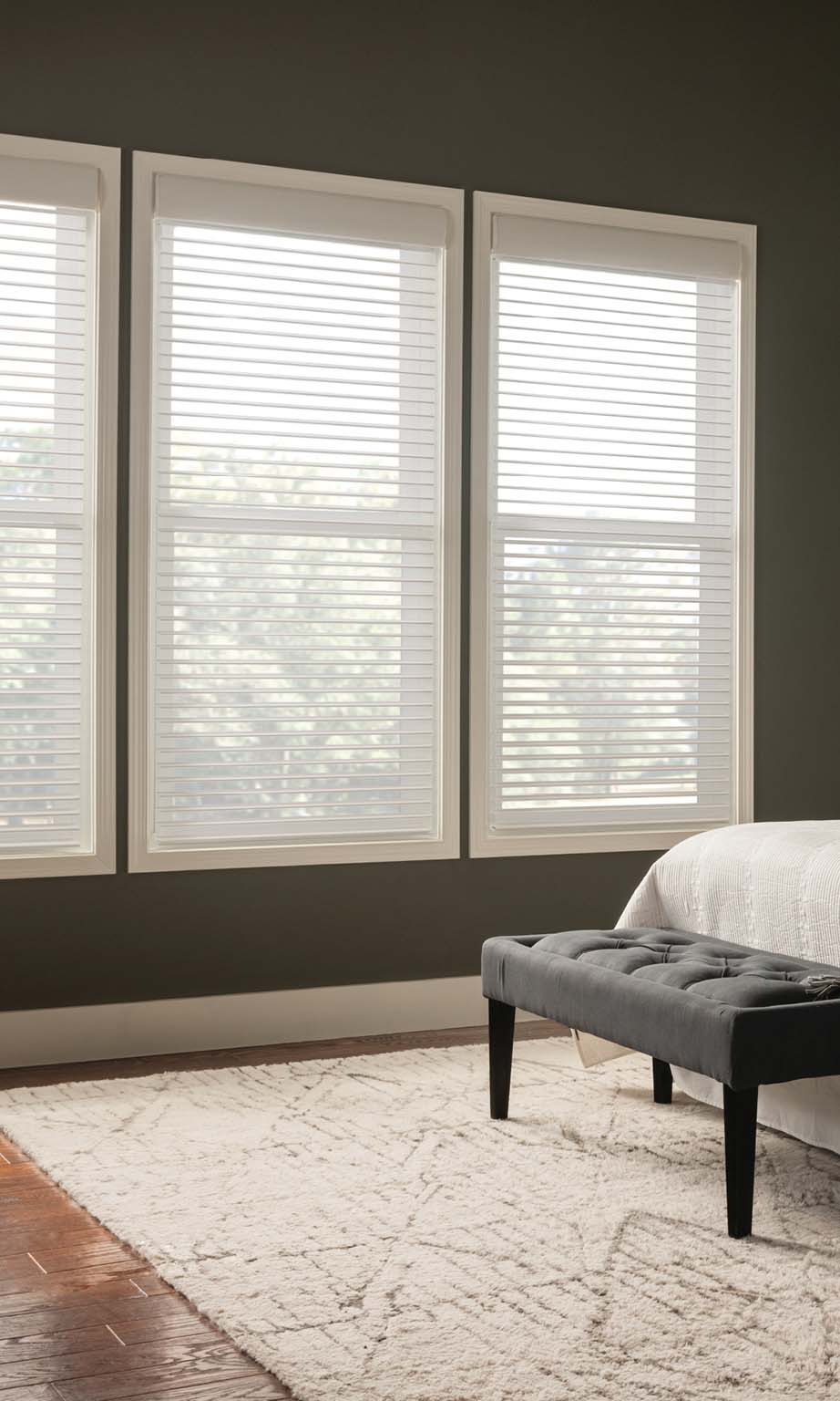 Three bedroom windows featuring white horizontal blinds and a grey bench