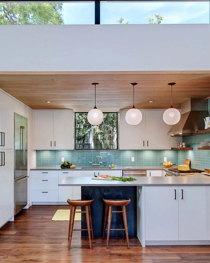 Bright kitchen with white cabinetry, teal tile backsplash, and three globe pendant lights