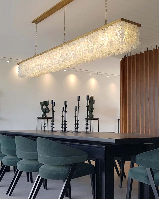 Long rectangular crystal chandelier hanging over a dark dining table with green velvet chairs