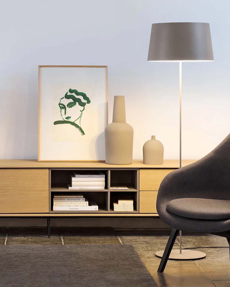 Minimalist floor lamp standing next to a wooden console table with art and decorative vases