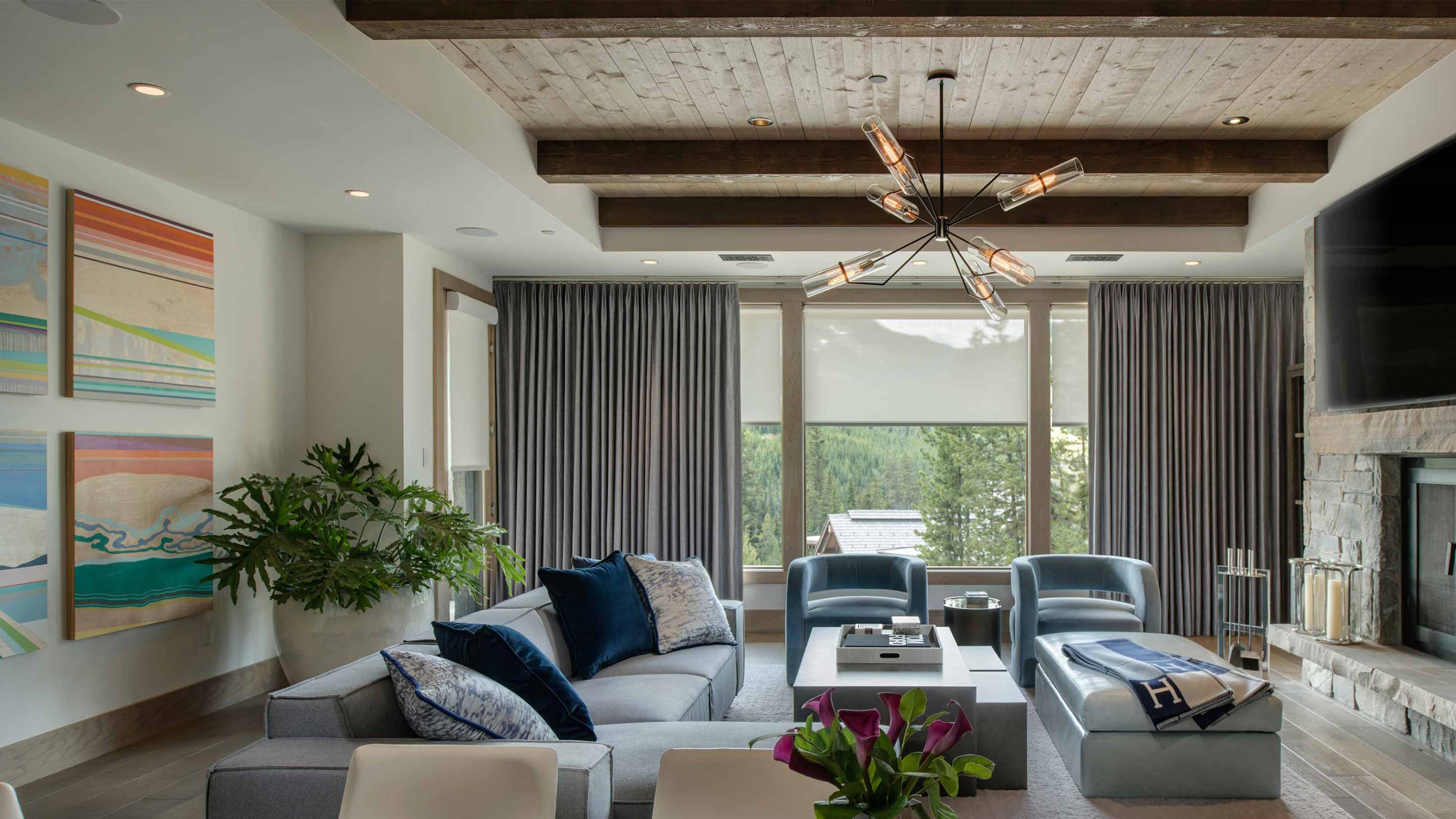 Modern living room with grey curtains and roller shades overlooking a forest