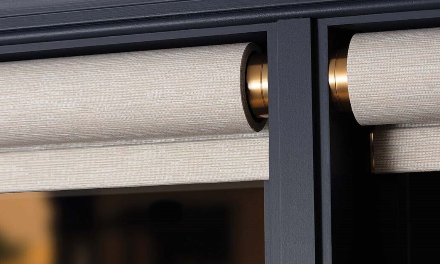 Close up of motorized roller shades with gold hardware mounted in a dark grey frame