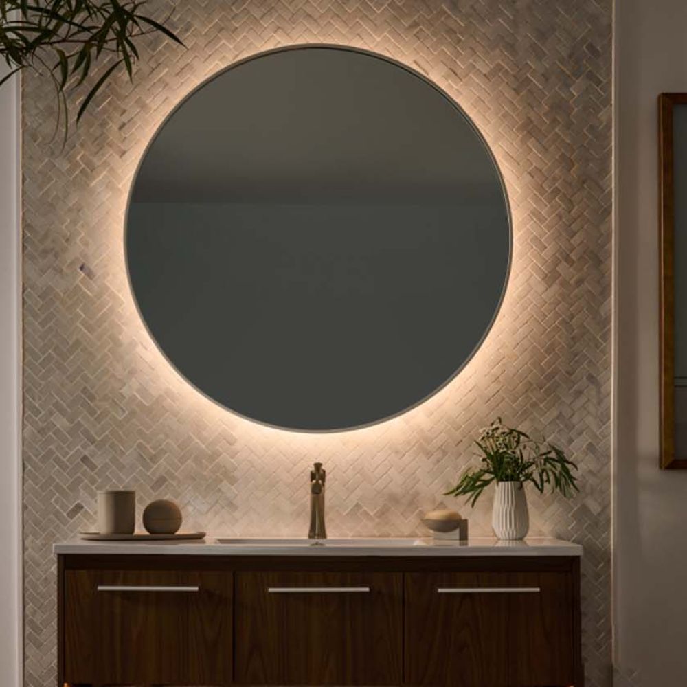 Round bathroom mirror with warm integrated halo backlighting against a herringbone tile wall